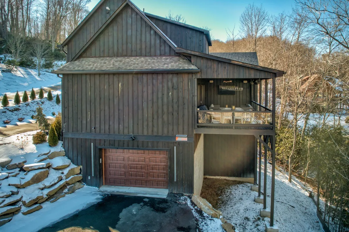This image showcases the exterior of the home with a clear view of the garage door, a balcony with seating, and a snowy, rustic setting. The garage is visibly accessible, and the scene evokes a peaceful, welcoming atmosphere perfect for both arrival and evening relaxation.