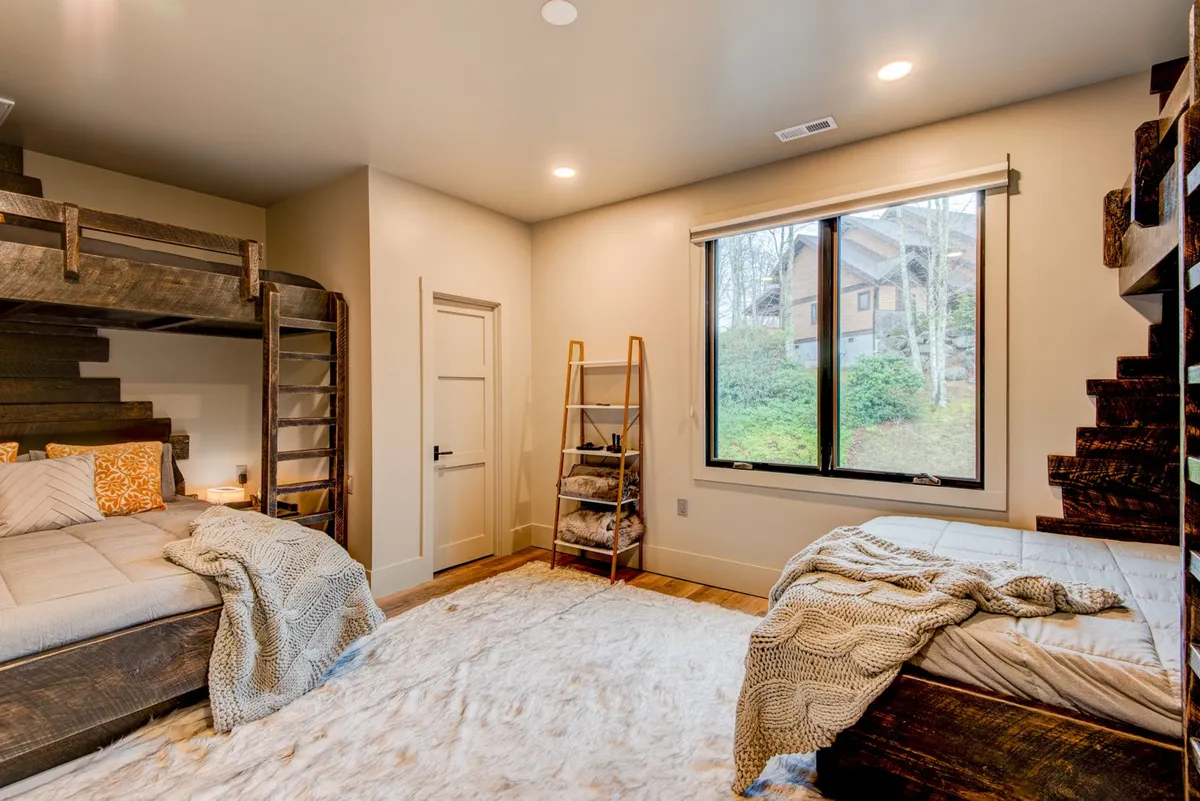 A playful and cozy bunk room with layered bedding, textured rugs, and a large window. The setup is perfect for kids or friends, offering a cheerful space for sleeping, playing games, or relaxing together.