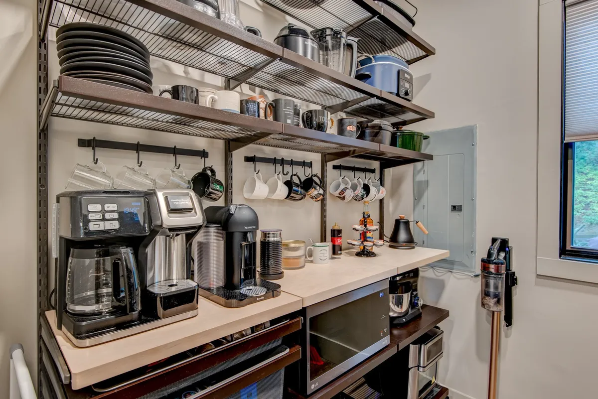 A practical, inviting interior shot featuring a coffee maker, shelves with dishes, a microwave, and hanging mugs. The space looks ready to greet guests with thoughtful starter amenities for a comfortable stay.