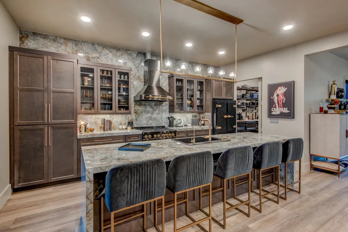 A bright, welcoming kitchen scene with a large island, modern appliances, and stylish cabinetry. Bar stools line one side of the island, creating a casual spot for breakfasts or evening wine. The overall design is both sophisticated and highly functional, emphasizing the kitchen as a hub for cooking and socializing.