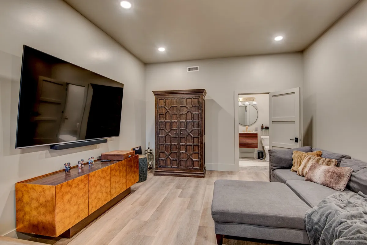 A comfortable sectional sofa faces a large flat-screen TV, with an ornate wooden cabinet and a relaxed, modern atmosphere. The space is clearly set up for cozy movie nights and social relaxation.