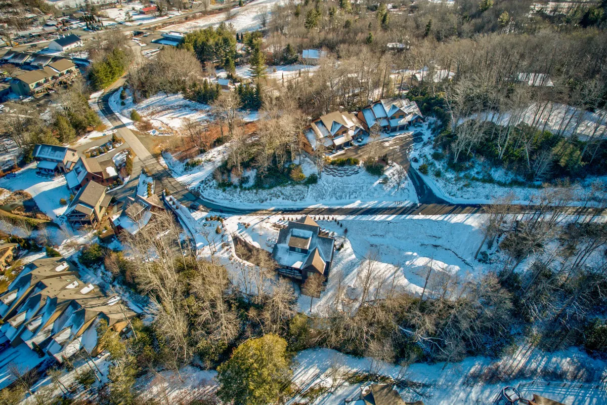 A peaceful view of a snow-covered landscape featuring a winding road, clusters of nearby houses, and tree-lined surroundings. The setting feels tranquil and showcases the broader community and recreational opportunities just beyond the home's doorstep.