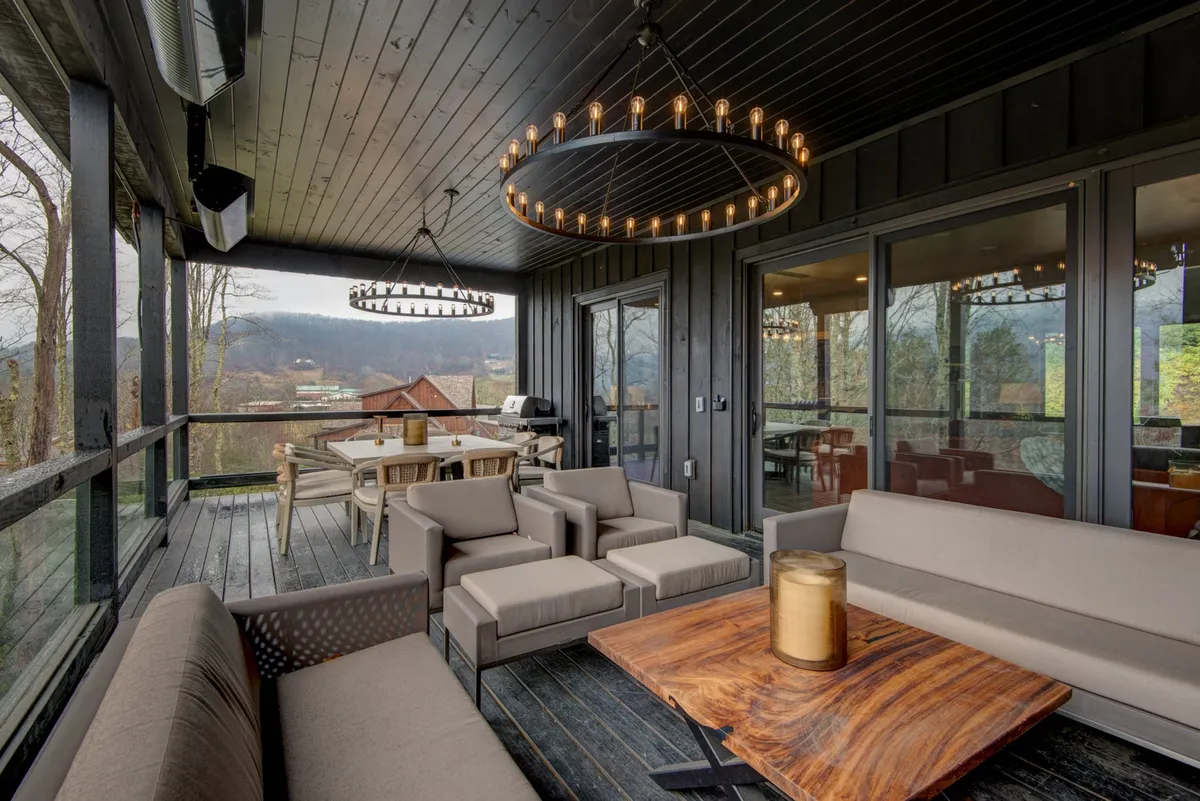 An inviting outdoor entertainment deck features chandeliers, stylish seating, a wooden dining table, and stunning mountain views. The setting is perfect for sunset dinners, stargazing, and social gatherings, all with a backdrop of natural beauty.