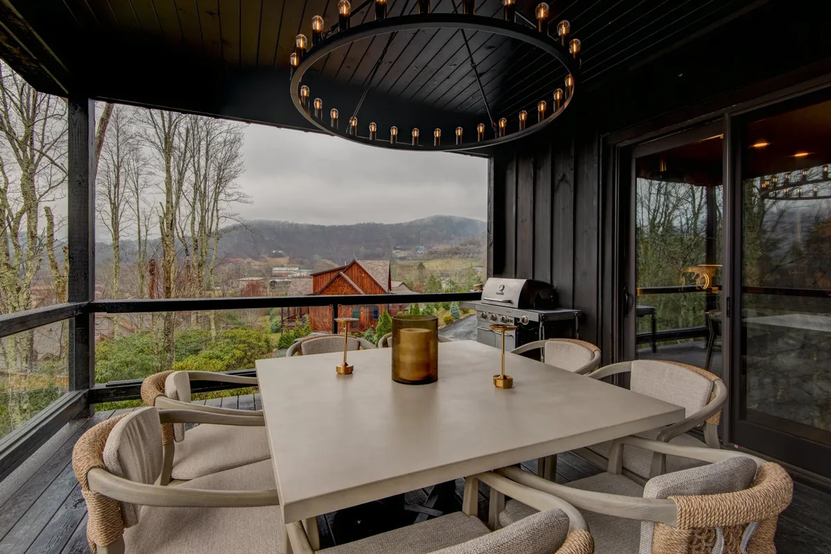 An outdoor communal dining area with a large concrete table, stunning circular chandelier, and panoramic views of the surrounding natural landscape. The setting suggests a relaxed, social environment ideal for family gatherings, outdoor meals, and watching sunsets.